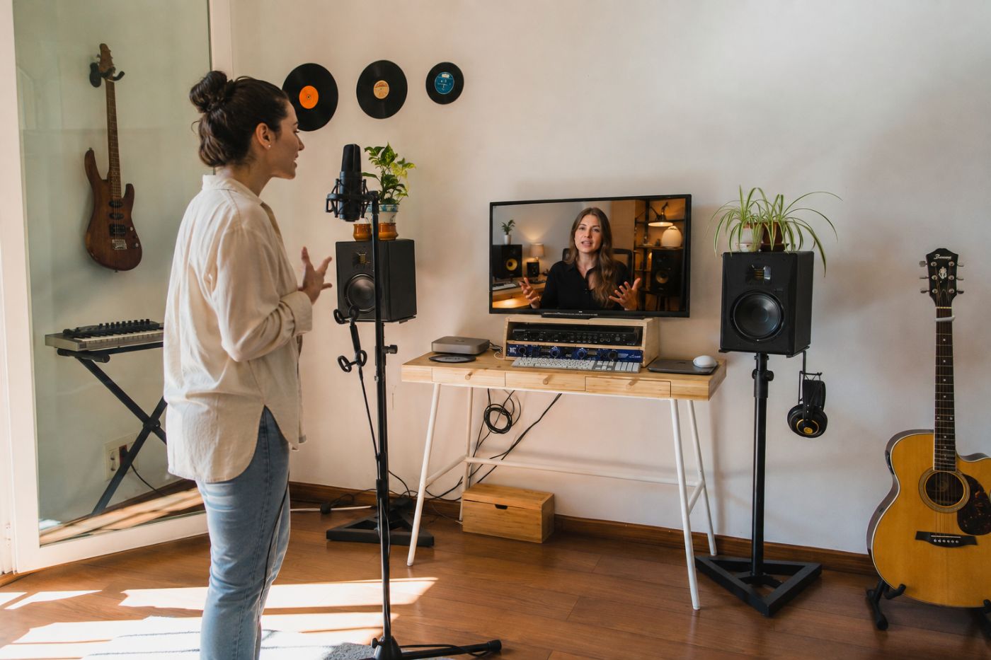 Una cantante entrena en una sala equipada con micrófono, monitores y pantalla, conectada con su coach a distancia.