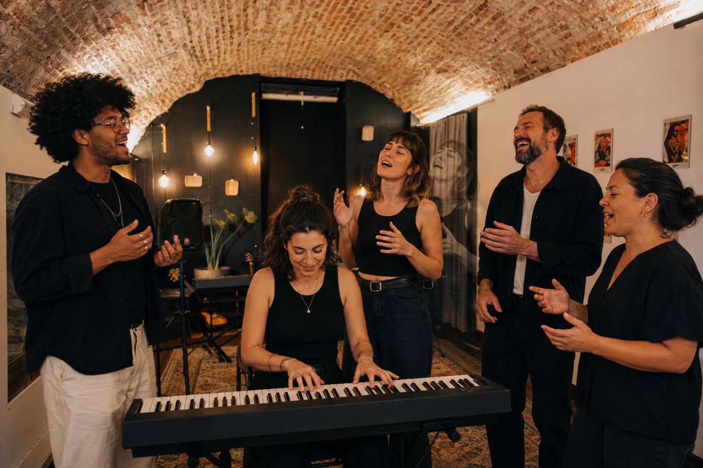Práctica colectiva: cinco personas de edades distintas cantan alrededor de un piano en una sala abovedada.
